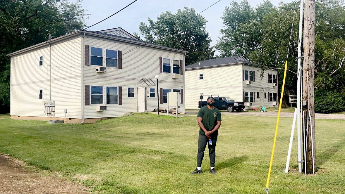 Man standing in front of a house with a green lawn and trees in the background