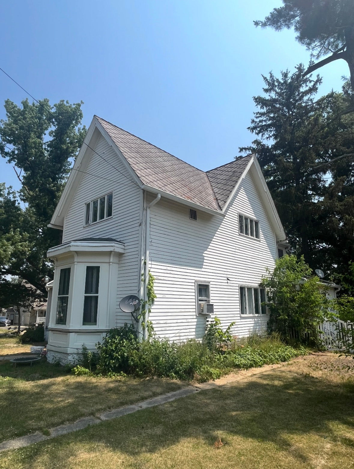 White house with a gray roof surrounded by trees on a sunny day
