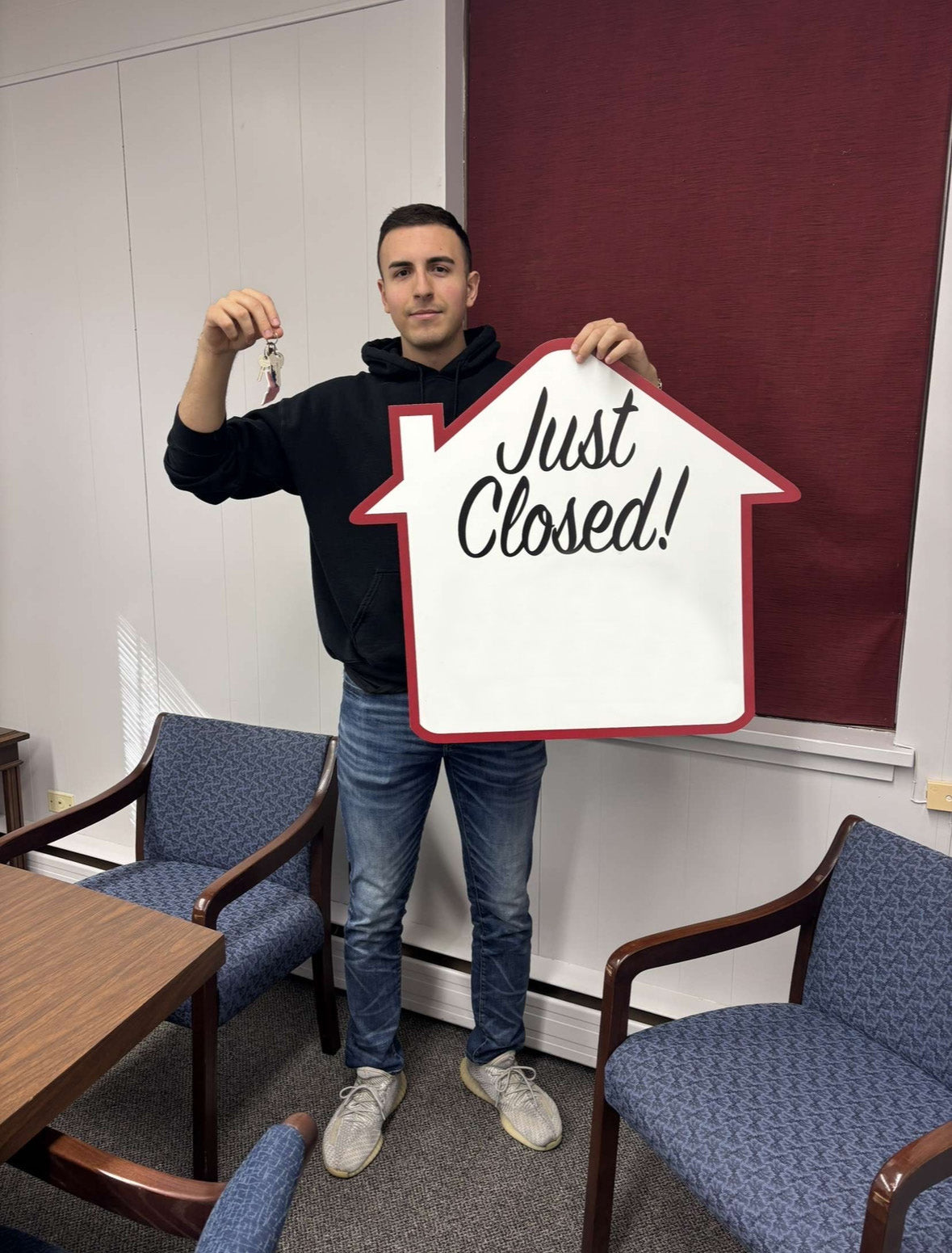 Man holding a house-shaped sign with 'Just Closed!' text in an office setting