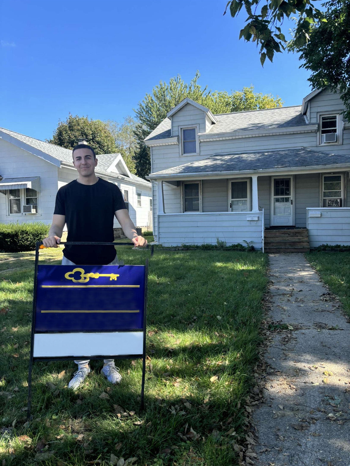 Person holding a yard sign with a key symbol in front of a house