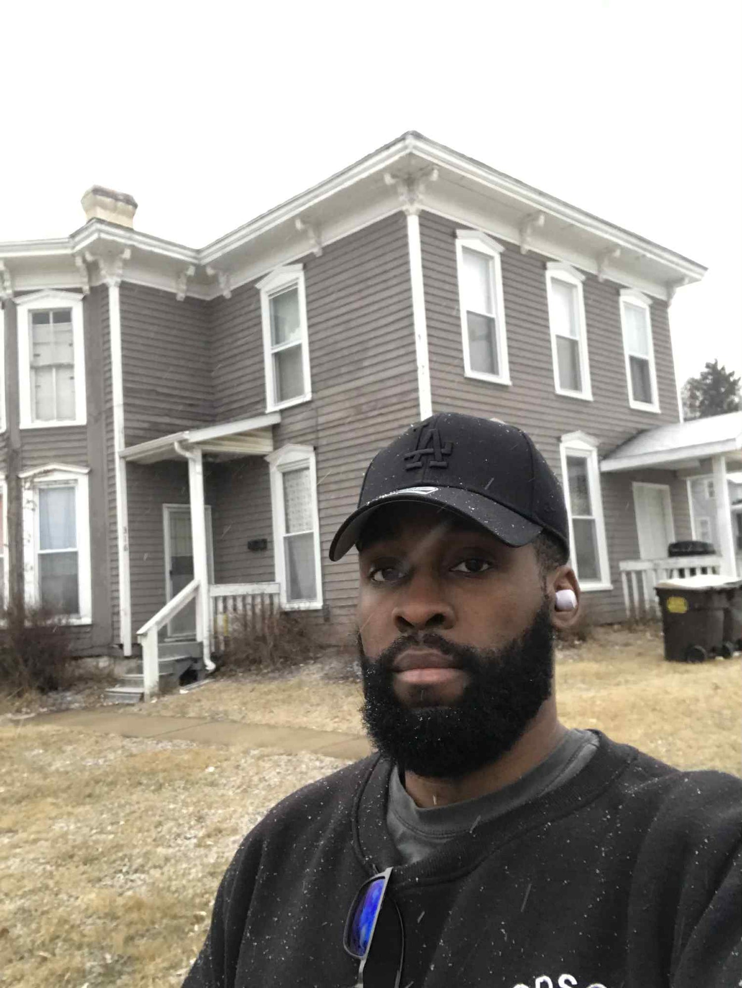 Man wearing a cap in front of a two-story house